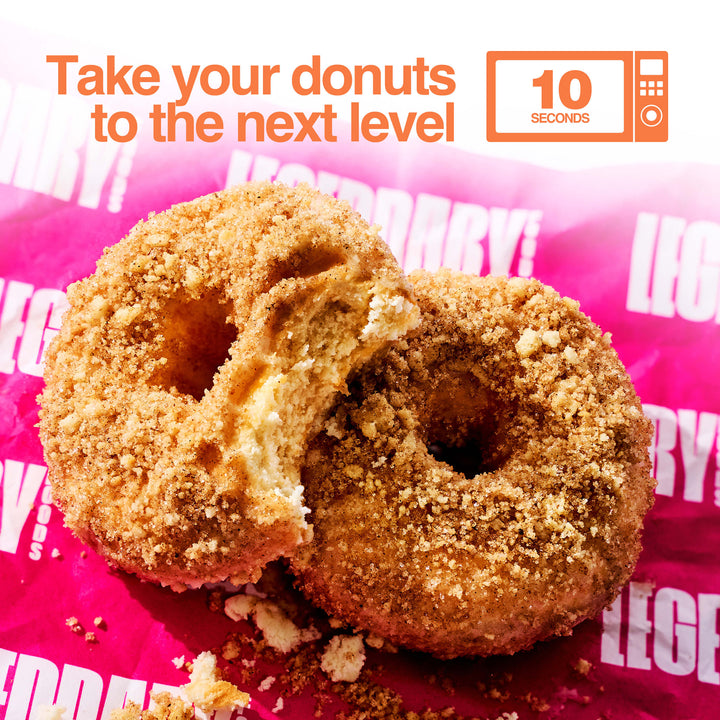 Two crumb-coated cinnamon donuts, one with a bite taken out, rest on pink Legendary Foods paper. Text reads “Take your donuts to the next level – 10 seconds” with a microwave icon.