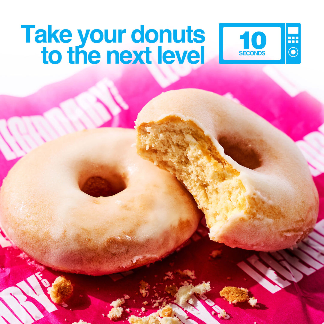 Two vanilla-glazed donuts, one with a bite taken out, on pink Legendary Foods paper. Text reads “Take your donuts to the next level – 10 seconds” with a microwave icon.
