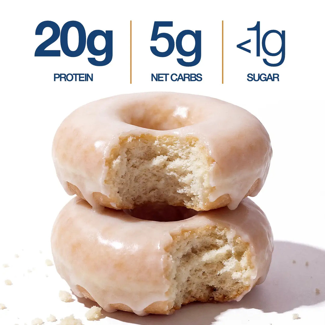 Two stacked Vanilla Glazed Mini Protein Donuts with bites removed, revealing their soft interior and glossy vanilla glaze. Contains 20g protein and 5g net carbs per serving.