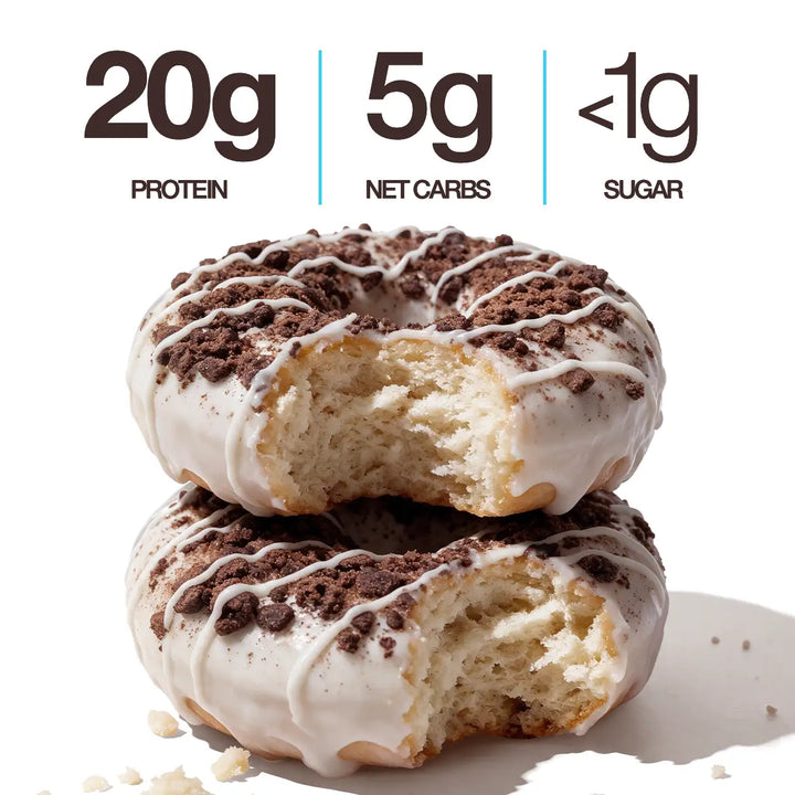 Two Cookies & Cream Mini Protein Donuts with white icing, chocolate cookie crumbles and white drizzle, shown with 20g protein, 5g net carbs and less than 1g sugar callouts.