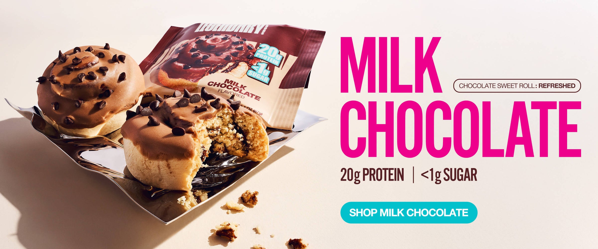 Two iced protein sweet rolls with chocolate chips on a tray beside branded packaging. Text highlights 20g protein, <1g sugar.