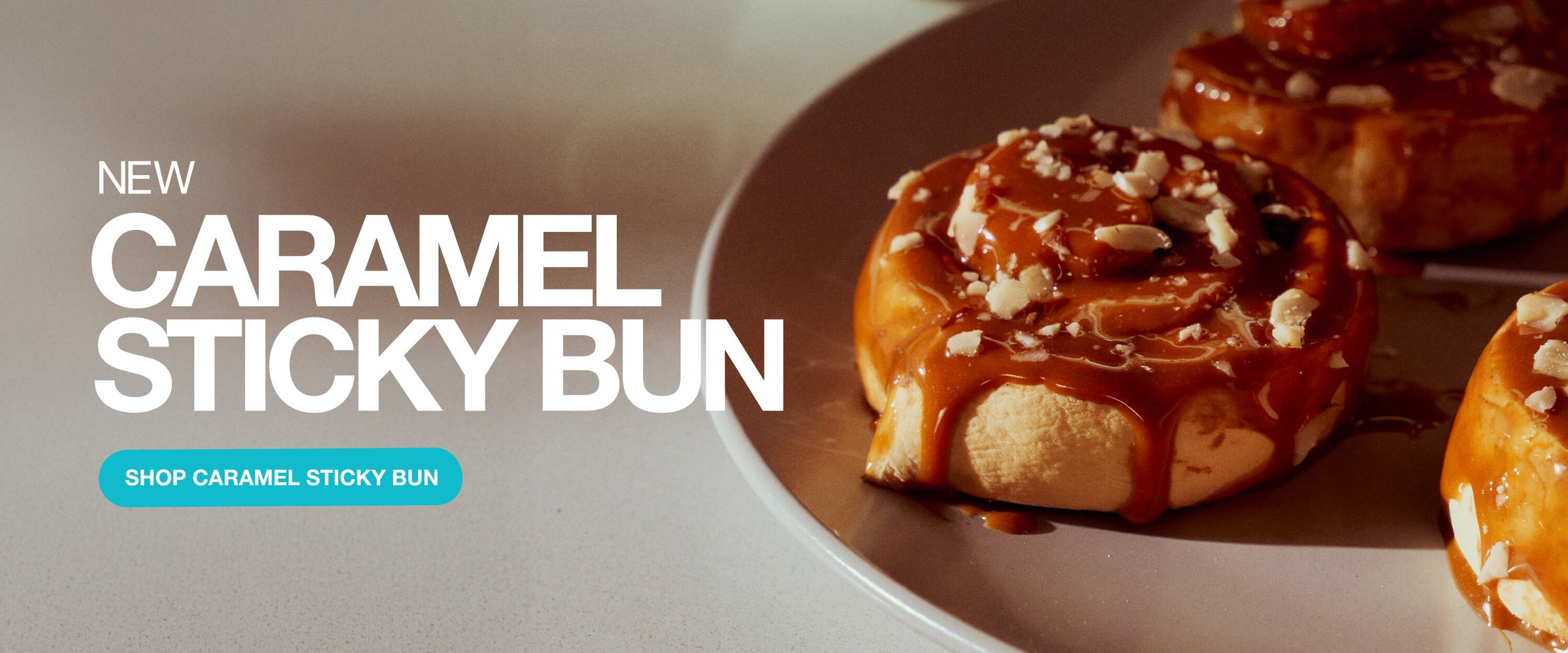 Wide banner showing caramel sticky buns on a plate with bold text “New Caramel Sticky Bun” and a teal button that says “Shop Caramel Sticky Bun.”