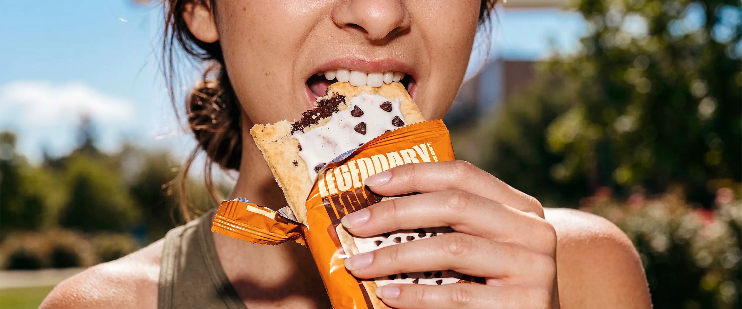 Person eating a smores protein pastry outdoors with trees in the background